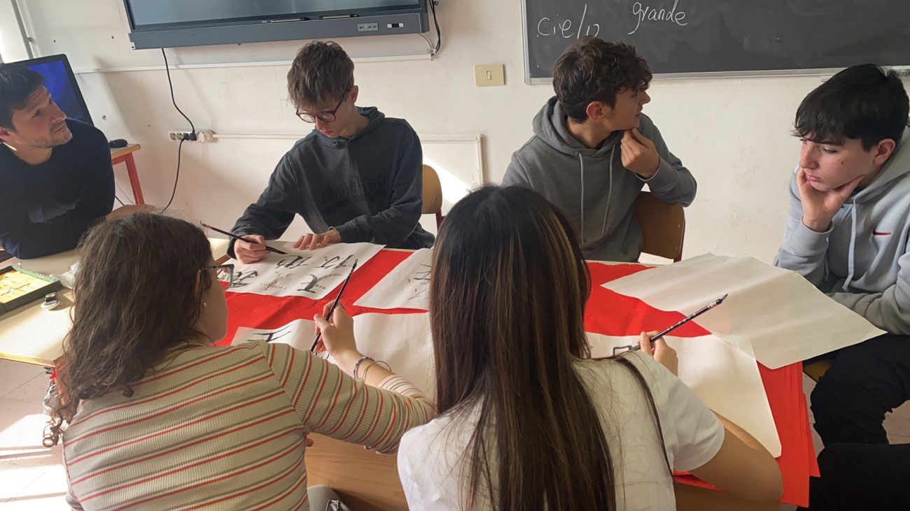 Studenti italiani praticano la calligrafia cinese durante una lezione scolastica a Prato.